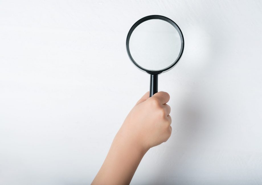 Magnifier in a children's hand on a white background. Close-up.